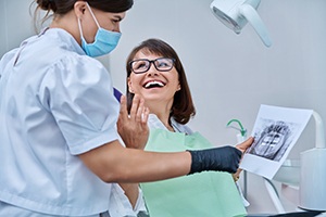 Patient smiling at dental assistant holding X-ray