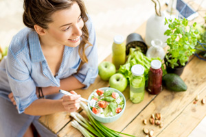 Bird’s eye view looking down at woman eating salad at table next to fruits and veggies