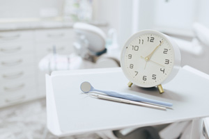 White clock on dental tray next to dental exam instruments