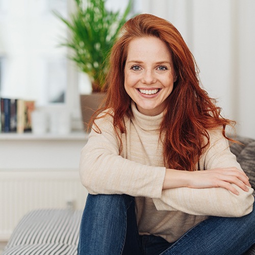 Red-haired woman in sweater smiling and sitting on couch