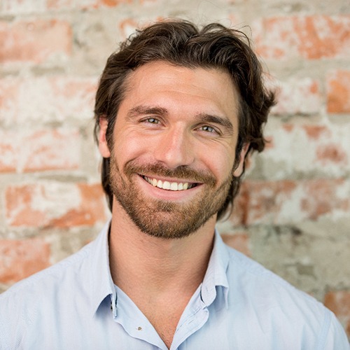 Man in collared shirt standing in front of a brick wall and smiling