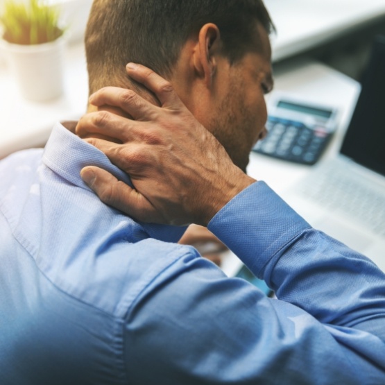 Man sitting at desk and rubbing back of his neck in pain