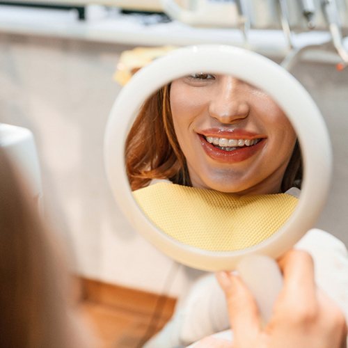 Woman smiling at reflection in handheld mirror