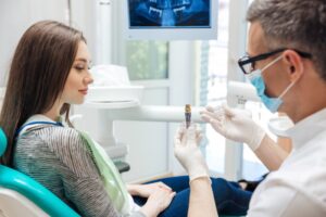Dentist showing young woman model of dental implant.
