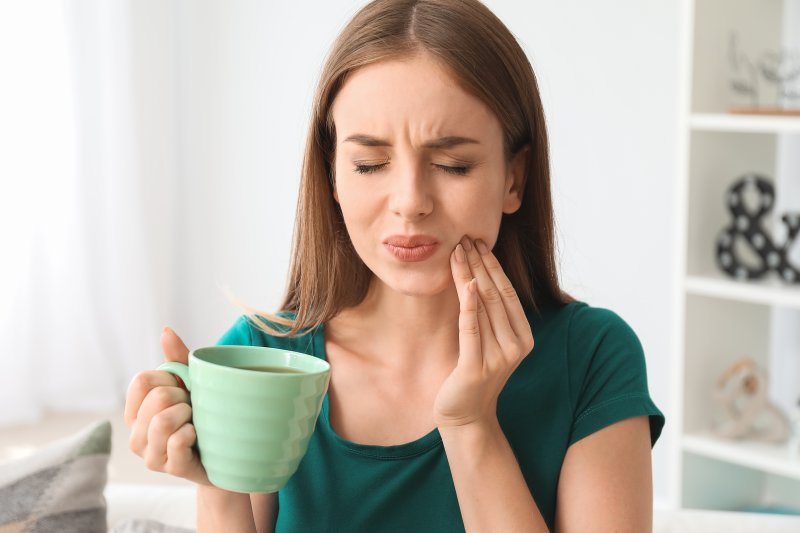A woman holding a mug of coffee and experiencing tooth pain