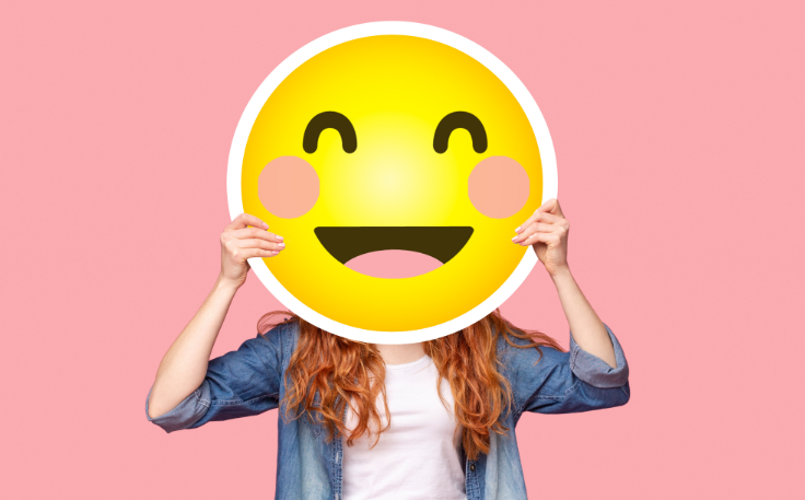 Woman holding smile emoji over face